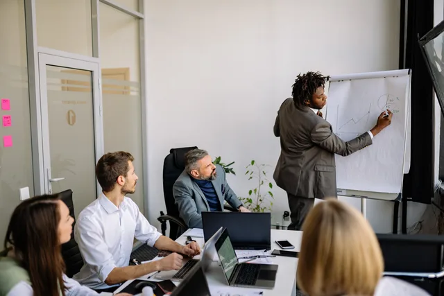A diverse team in a modern office engaged in a strategic business meeting led by a presenter. How to map prospecting software AI applications to real sales tasks