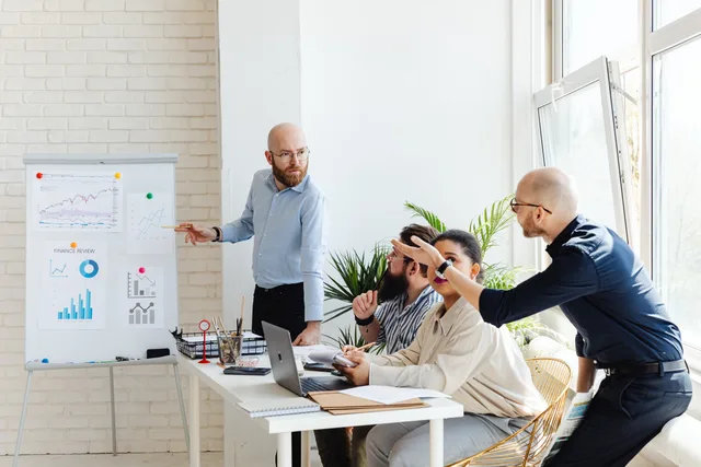 A group of professionals engaged in a business meeting, discussing financial graphs on a whiteboard. What the best prospecting software providers mean for England buying teams