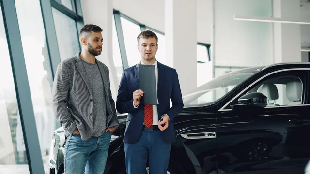 Two businessmen discussing car purchase in modern dealership showroom. Should my sales team own its prospecting channels or rent an audience?