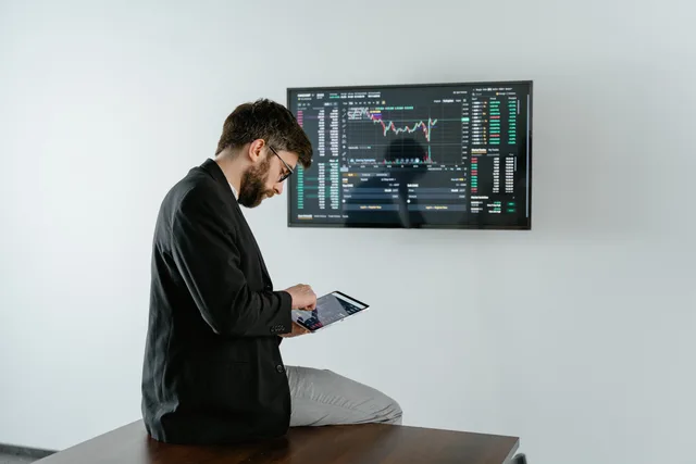 Young man in office analyzing financial graphs on a tablet with stock market screen displayed. Skills planning for lead generation software teams